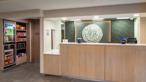 A reception area with a wooden reception desk, a decorative wall piece, and a vending machine stocked with snacks and drinks. - Fairfield Inn & Suites By Marriott Memphis Germantown (Germantown)