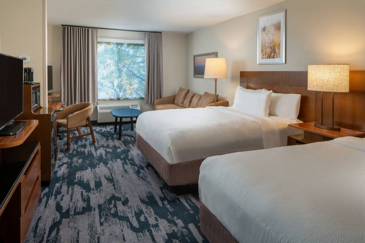 A hotel room with two beds, a desk, a chair, a TV, and a window with curtains.