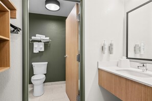 A modern bathroom with a white sink, mirror, and toilet. There are towels on a rack and toiletries on the counter. - Spark by Hilton Traverse City (Traverse City)