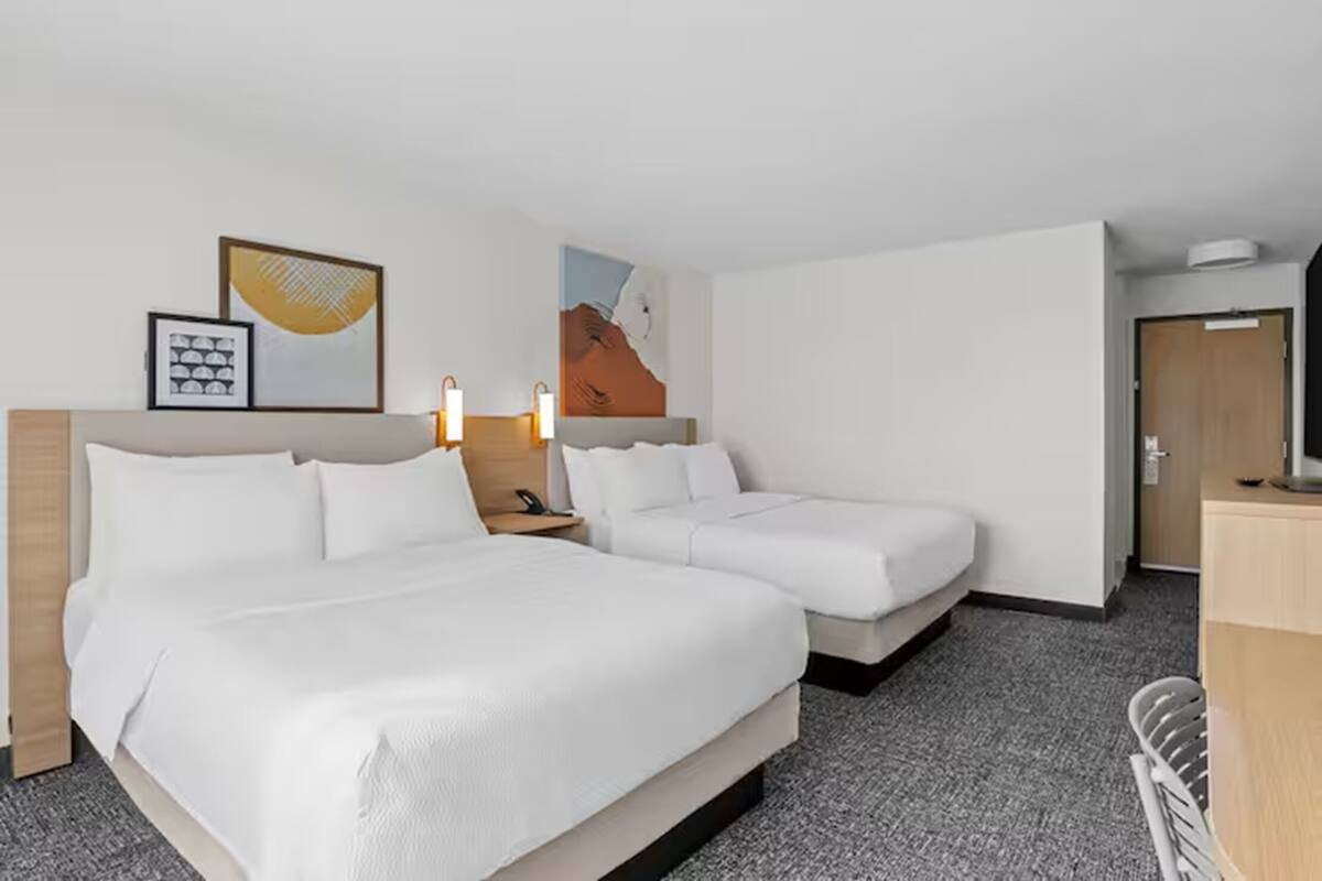 A hotel room with two beds, a desk, a chair, and artwork on the walls.