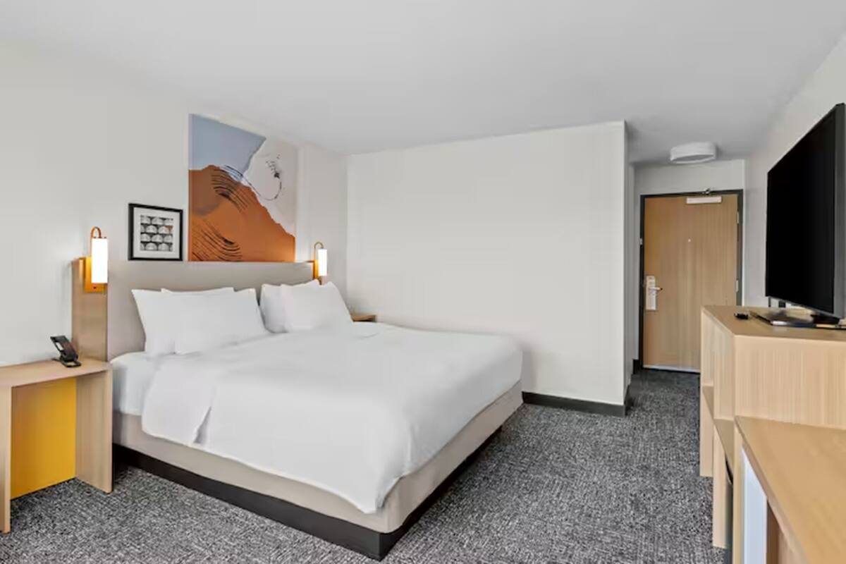 A hotel room with a bed, bedside tables, a TV, and a door.
