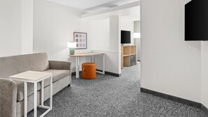 A hotel room with a sofa, a small table, a lamp, a TV, and a trash bin.
