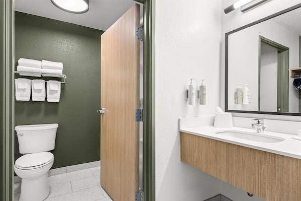 A modern bathroom with a toilet, a sink, and a mirror. There are towels hanging on a rack and toiletries on the sink counter.