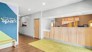 A modern reception area with a wooden reception desk, a green carpet, and a wall with a geometric design and a motivational quote.