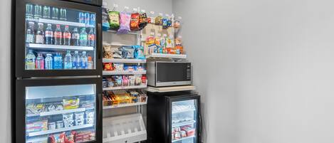 A vending area with a refrigerator, microwave, and shelves stocked with snacks and beverages.