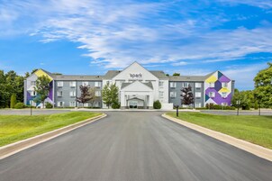 Un hotel de varios pisos con una entrada central, rodeado de céspedes cuidados y un cielo despejado.