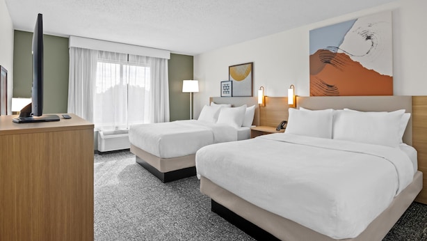 A hotel room with two beds, a flat-screen TV, a desk, and a window with curtains.