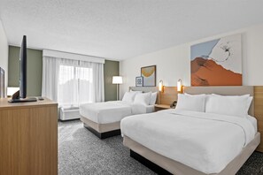 A hotel room with two beds, a flat-screen TV, a desk, and a window with curtains.