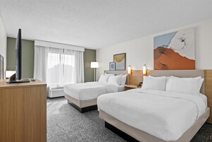 Habitación de hotel con dos camas, una televisión de pantalla plana, un escritorio y una ventana con cortinas.