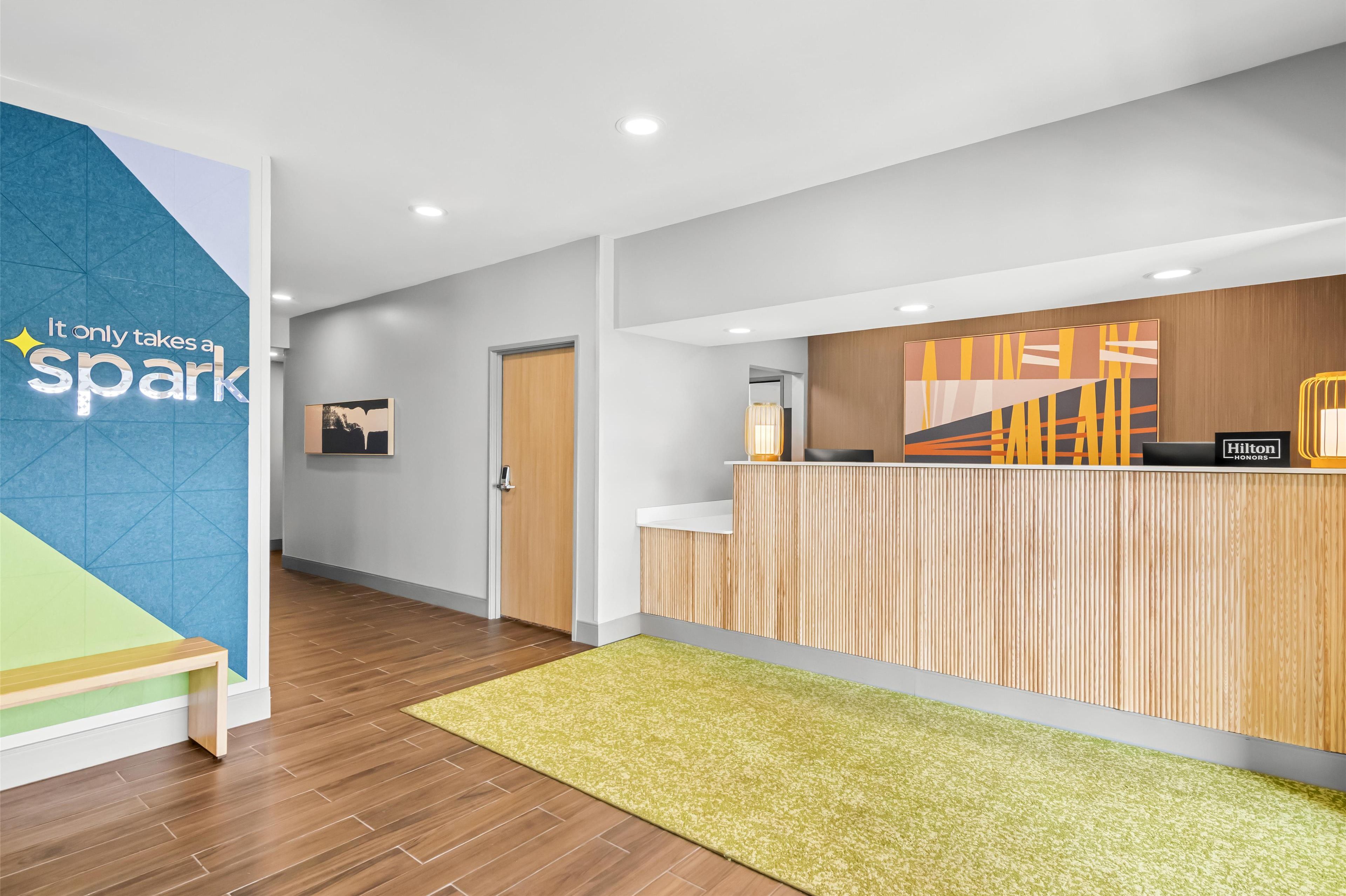 A modern reception area with a wooden reception desk, a green carpet, and a wall with a geometric design and a motivational quote.