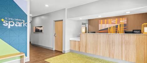A modern reception area with a wooden reception desk, a green carpet, and a wall with a geometric design and a motivational quote.