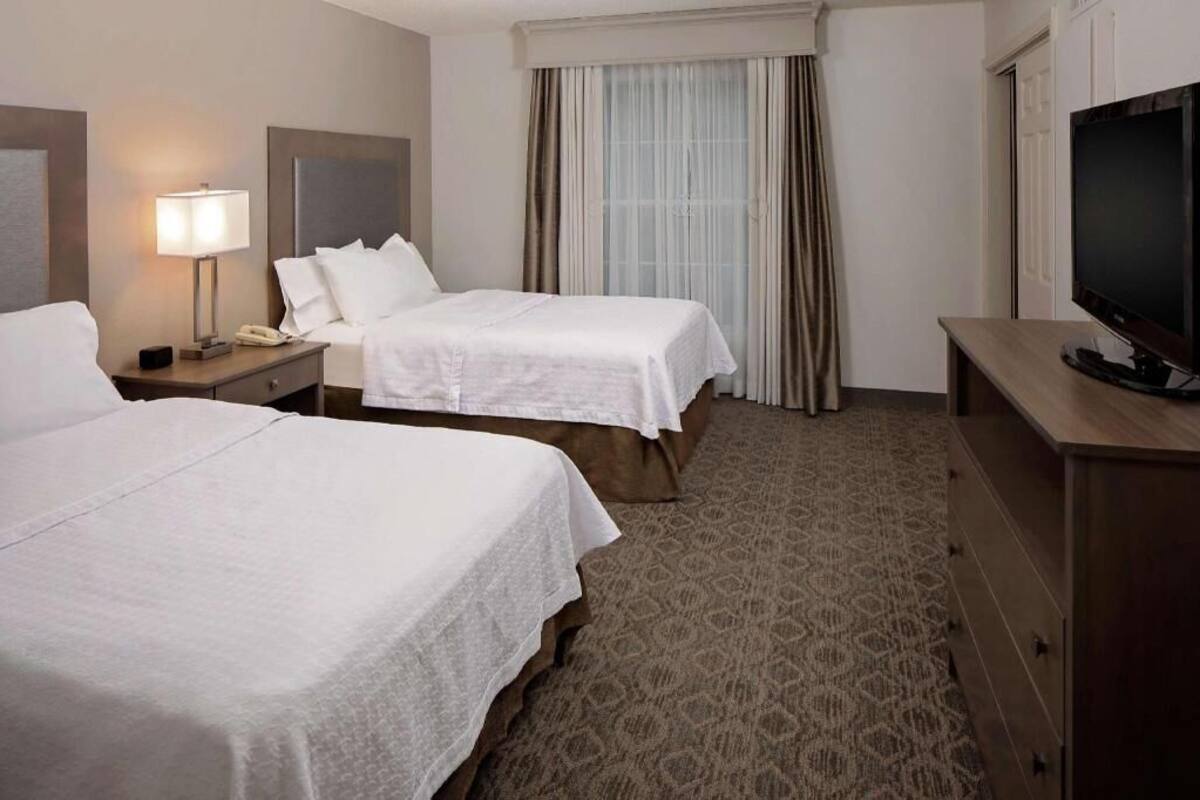 Une chambre d’hôtel avec deux lits, une télévision, une lampe, un téléphone et une fenêtre avec des rideaux.