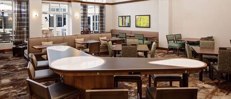 A spacious lobby with a central bar area, multiple seating options including sofas and chairs, and large windows providing natural light.