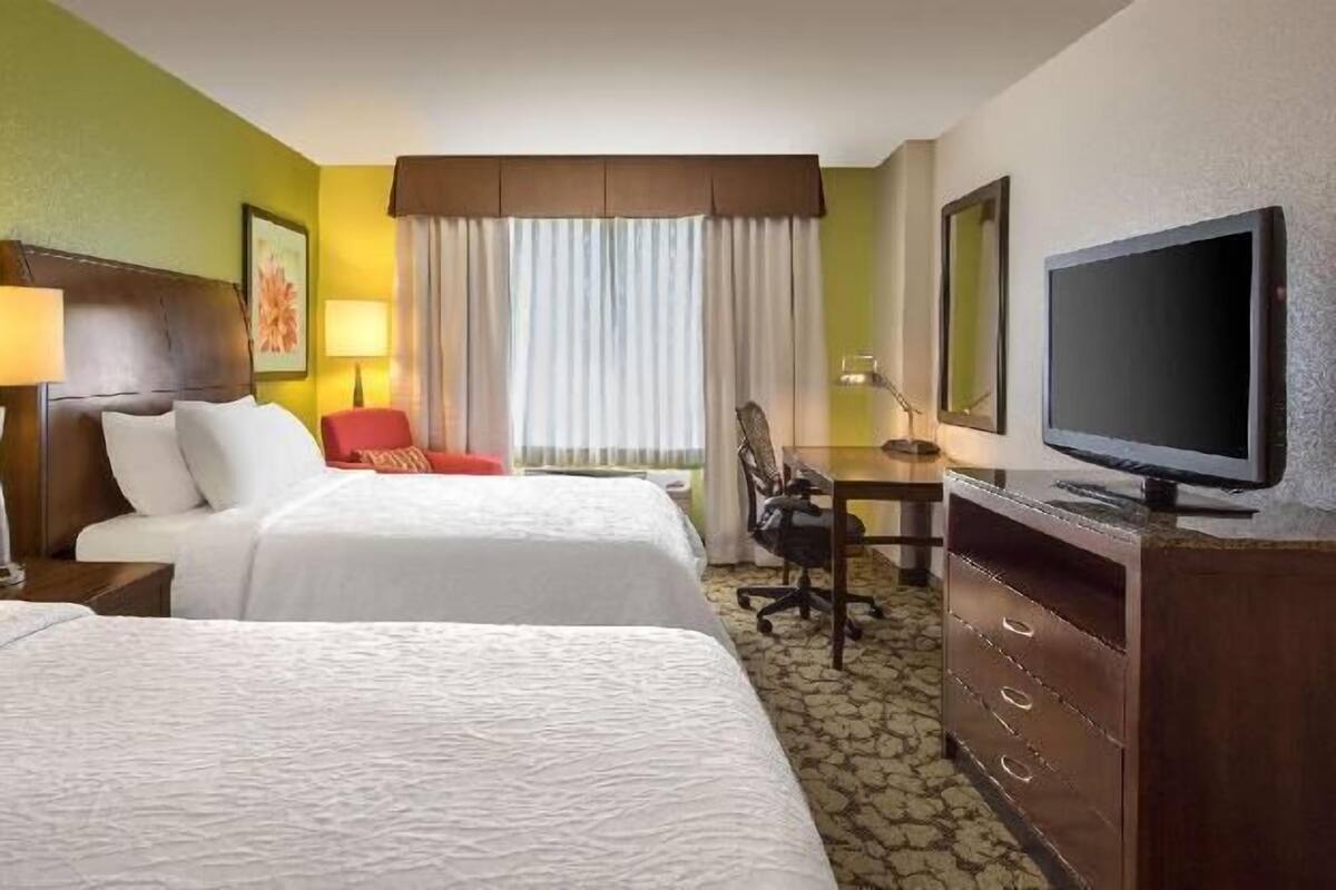 Hotelkamer met twee bedden, een bureau, een stoel, een televisietoestel en een raam met gordijnen.