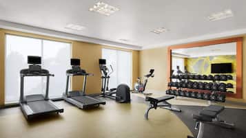 Un gimnasio con cintas de correr, elípticas, una bicicleta estática y un estante con mancuernas.