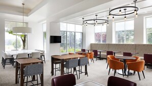 A spacious dining area with multiple tables and chairs, large windows, and modern pendant lighting. - Hilton Garden Inn Denver South Park Meadows Area (Englewood)