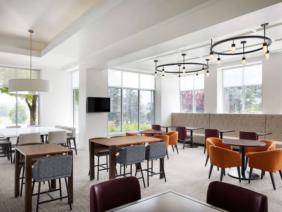 Un comedor amplio con varias mesas y sillas, ventanas grandes e iluminación colgante moderna.