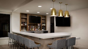 A modern bar area with a white countertop, bar stools, a wine rack, and a flat-screen TV mounted on the wall. - Hilton Garden Inn Denver South Park Meadows Area (Englewood)