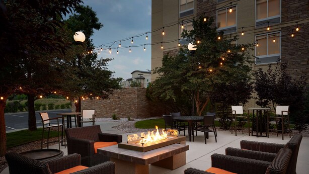 An outdoor patio area with wicker furniture, a fire pit, string lights, and a stone wall. - Hilton Garden Inn Denver South Park Meadows Area (Englewood)