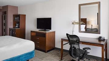 A hotel room with a bed, a desk with a chair, a television, a wardrobe, and a mirror.
