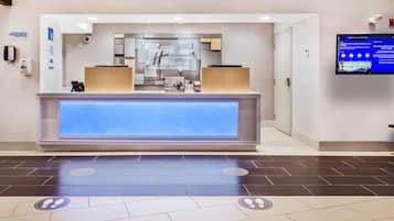 Een hotel receptie met een digitaal scherm waarop nieuws en evenementen worden getoond, een receptiebalie en een bord dat aangeeft dat alcoholische dranken niet zijn toegestaan in openbare ruimtes.