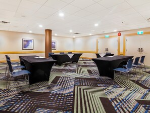 A conference room with tables and chairs, a patterned carpet, and a ceiling with recessed lighting.