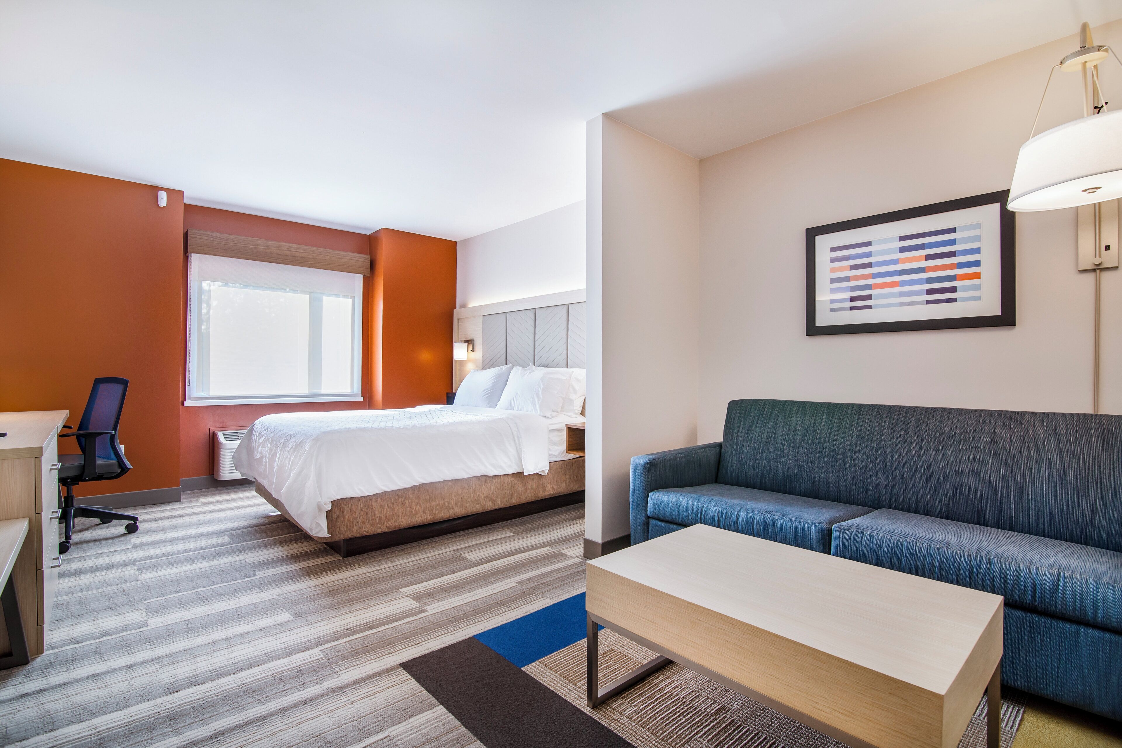 Una habitación de hotel con cama, escritorio, silla, sofá y lámpara.