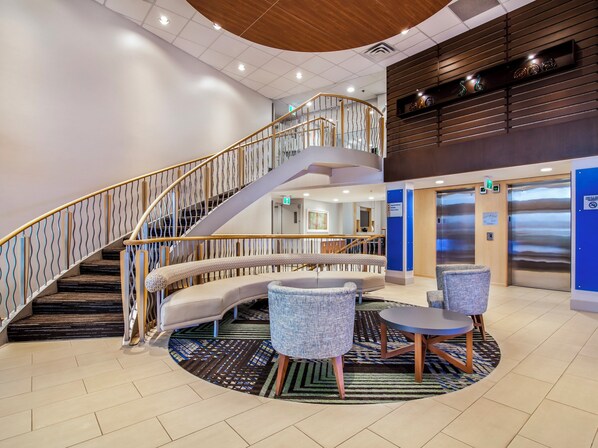 A lobby with a curved staircase, seating area, and a reception desk.