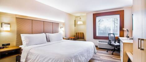 A hotel room with a bed, bedside table, desk, chair, and a window.