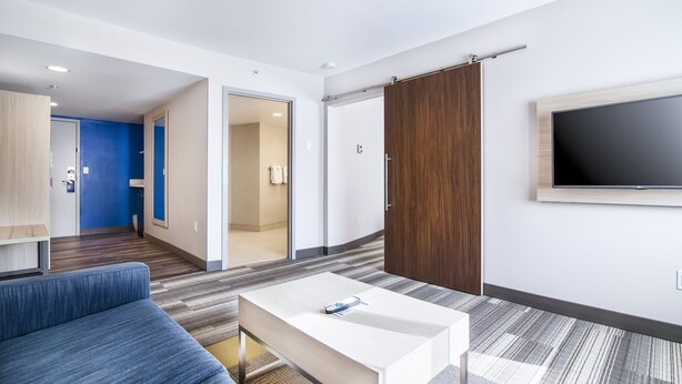 Ein modernes Hotelzimmer mit einer Couch, einem Couchtisch, einem an der Wand montierten Fernseher und einer Schiebetür zu einem Badezimmer.