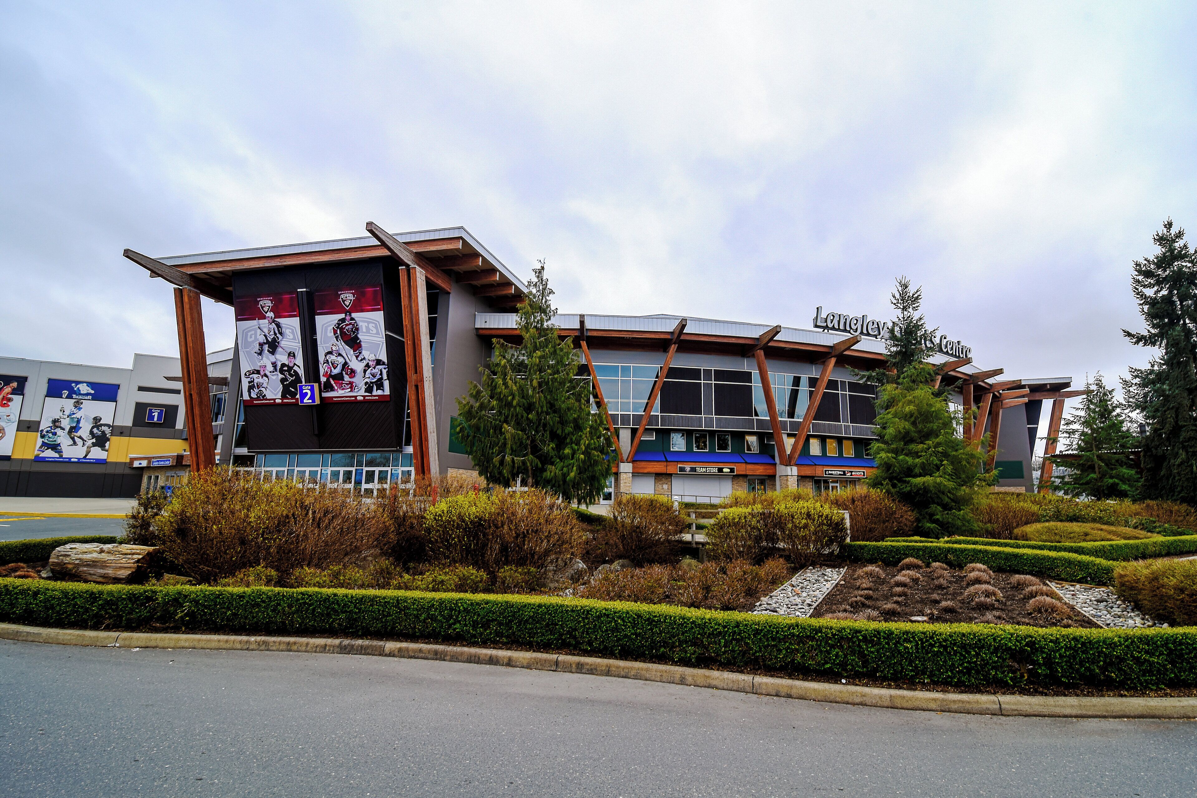 A modern building with a sports center sign, surrounded by landscaped gardens and a parking area.