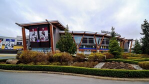 A modern building with a sports center sign, surrounded by landscaped gardens and a parking area.