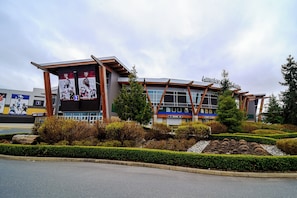 Un bâtiment moderne, sur lequel on peut voir une enseigne indiquant la présence d’un centre sportif, entouré de jardins aménagés et d’un espace de stationnement.