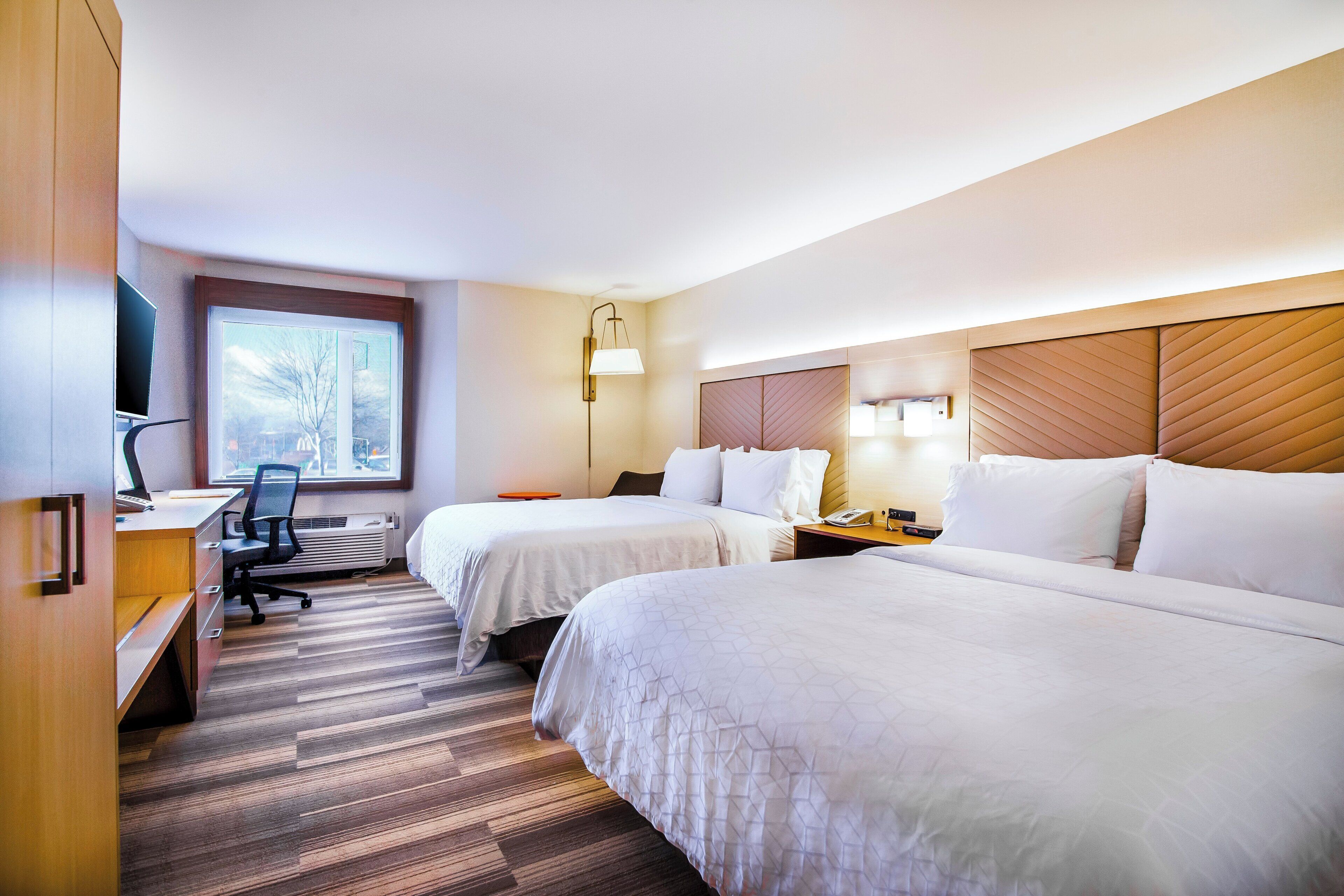 A hotel room with two beds, a desk with a chair, a TV, and a window.