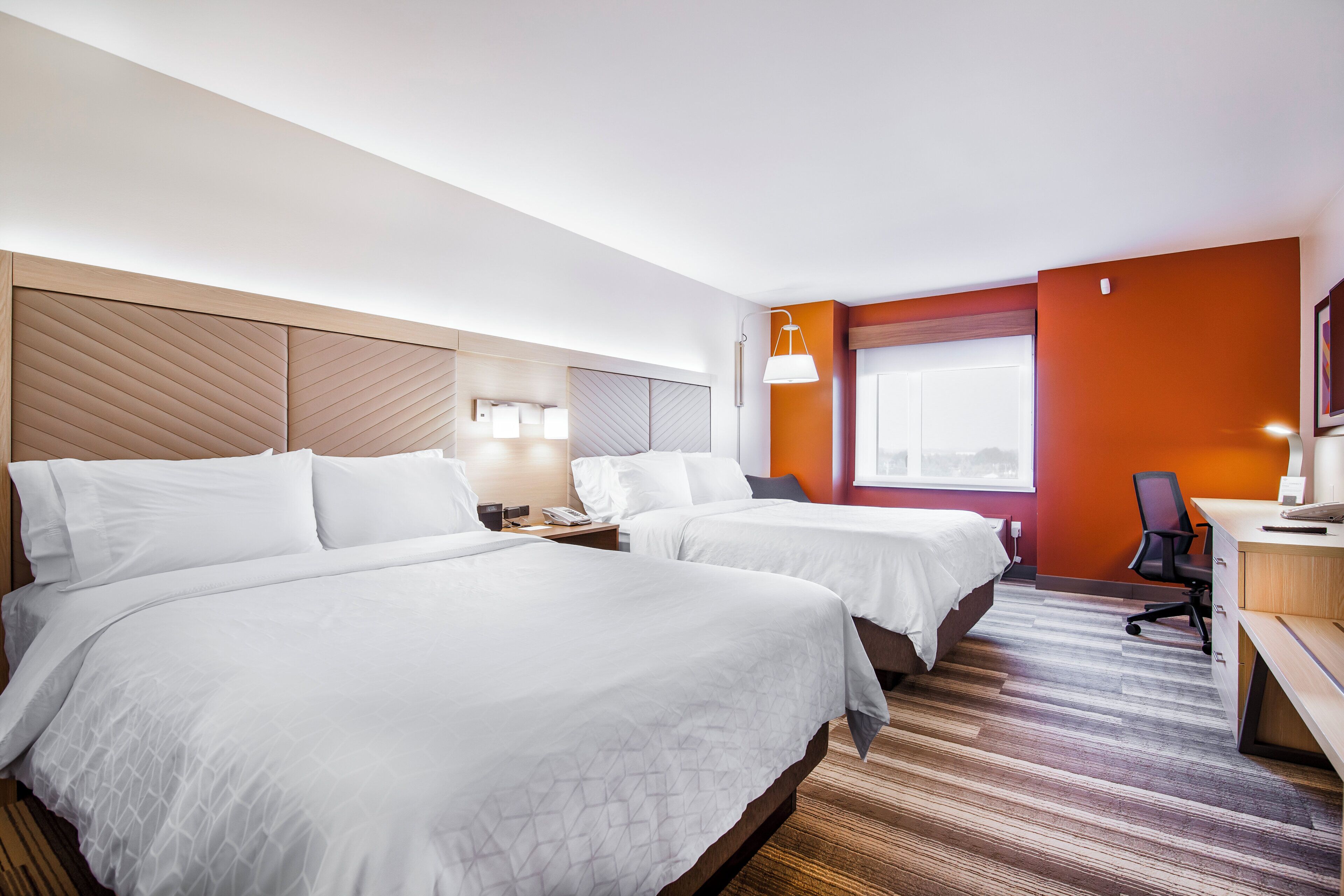 A hotel room with two beds, a desk, a chair, a window, and a modern lamp.