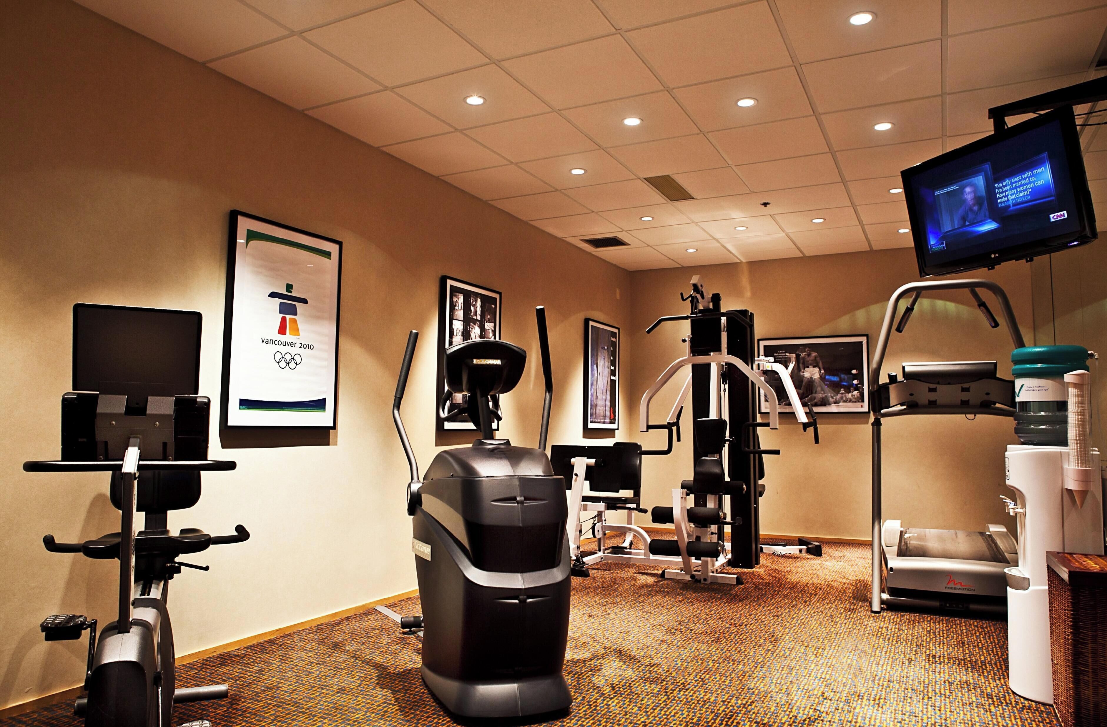 Un gimnasio con equipamiento de ejercicio, un televisor y cuadros en las paredes.