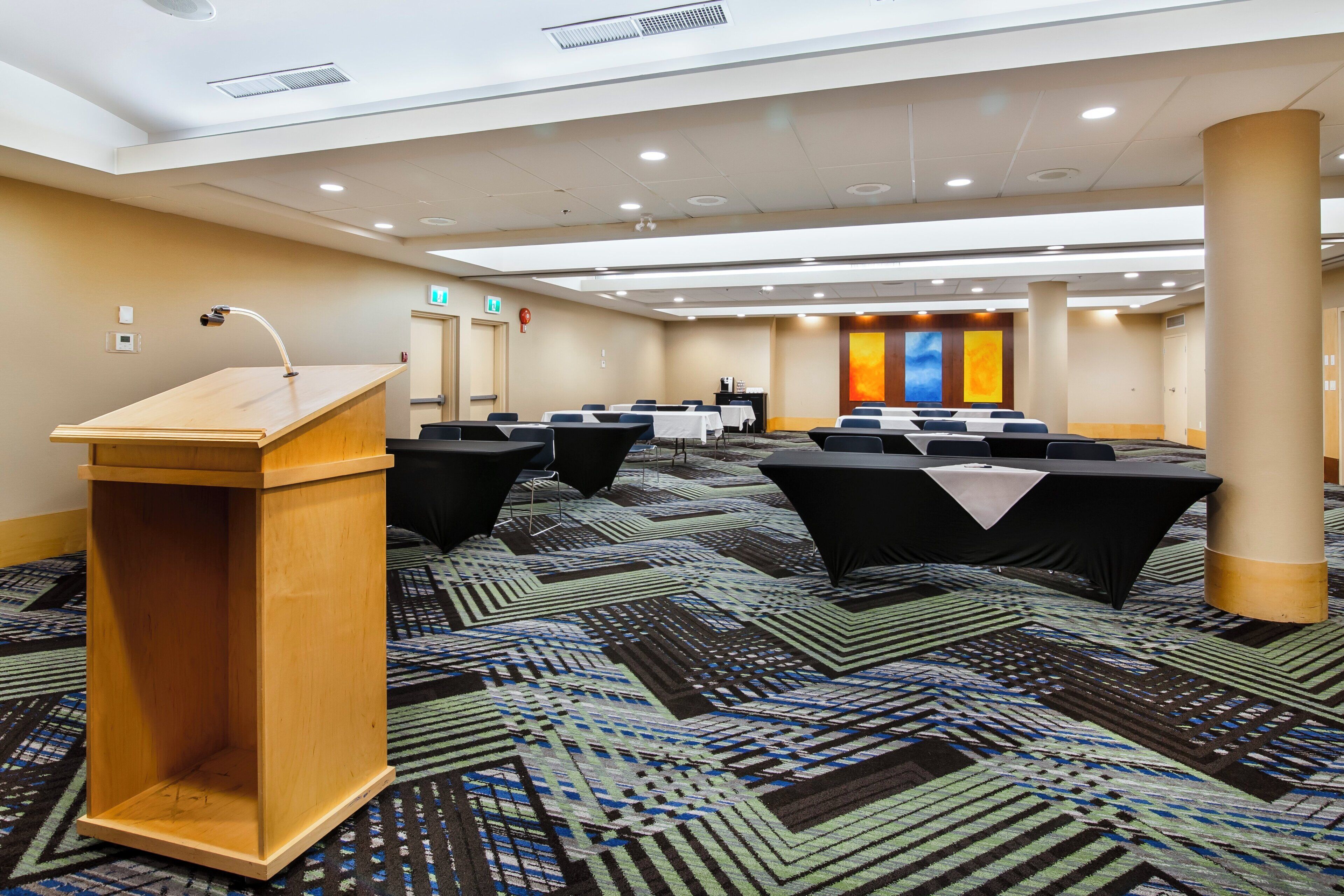 A conference room with a podium, tables, chairs, and a patterned carpet.