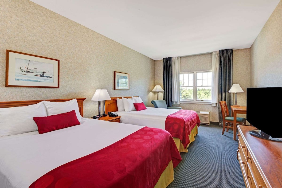 A hotel room with two beds, a desk, a television, and a window with curtains.
