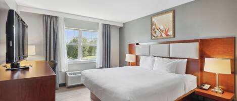 Habitación de hotel con una cama grande, un escritorio, un televisor y una ventana con cortinas.