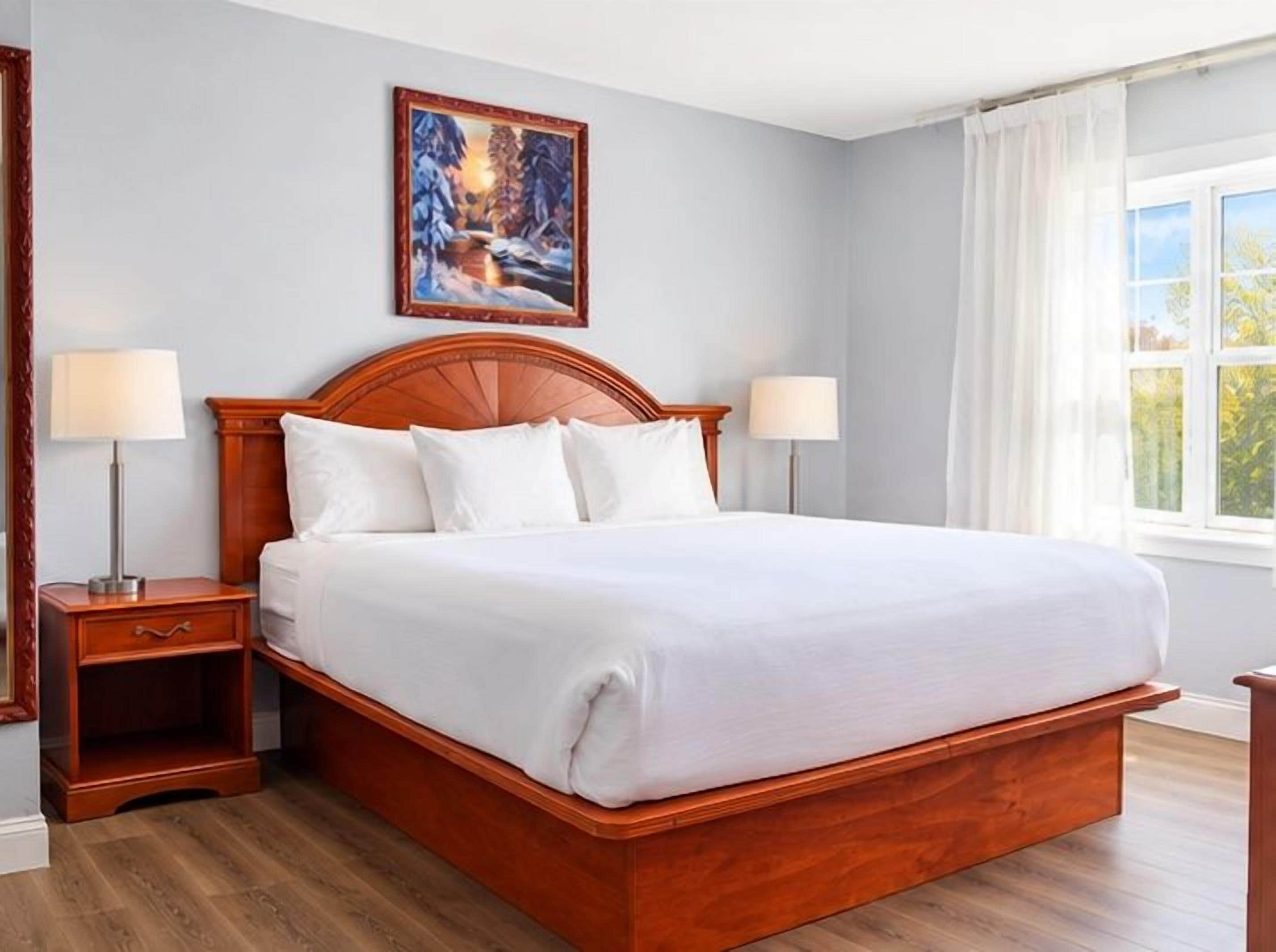 A large bed with a wooden headboard, two bedside tables, and a painting on the wall.