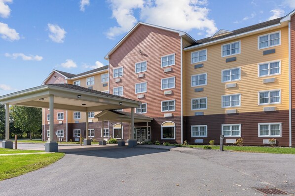 A multi-story hotel with a covered entrance, multiple windows, and a parking area.