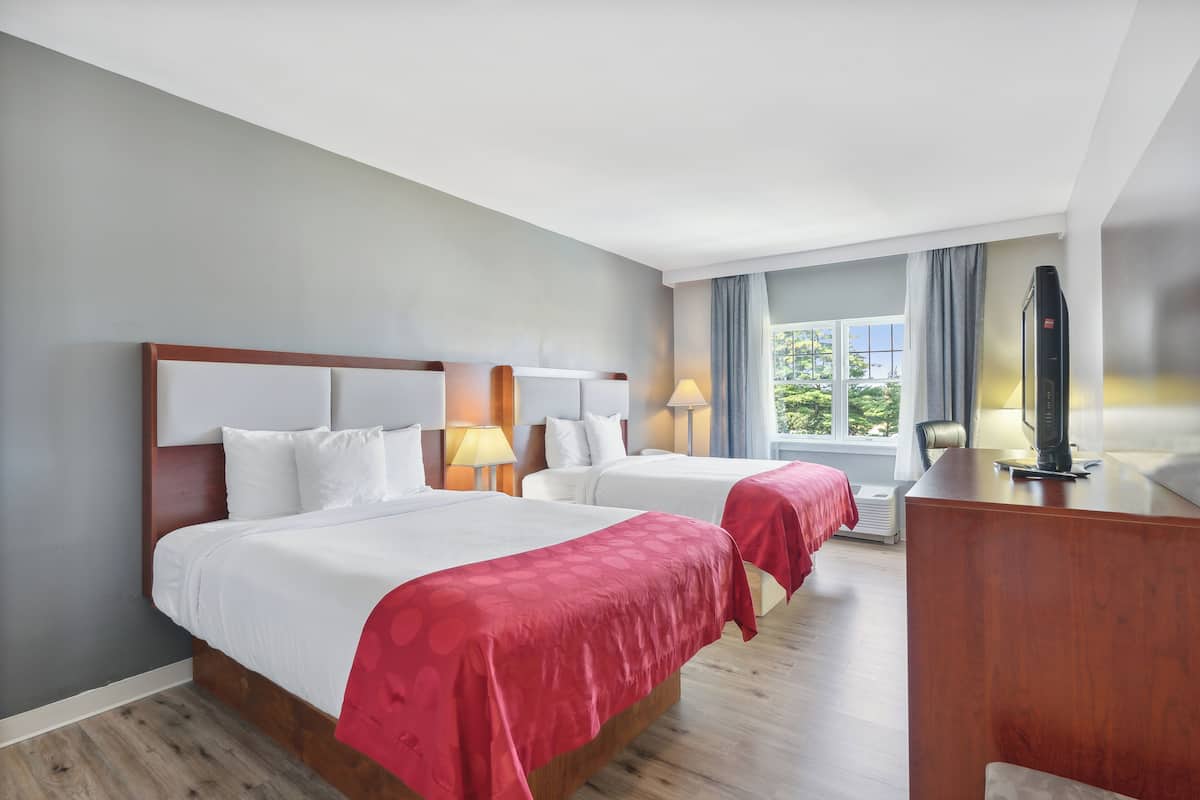 A hotel room with two beds, a desk, and a large window with curtains.