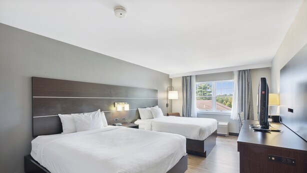 A hotel room with two beds, a desk, a TV, and a window with curtains.