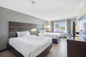 A hotel room with two beds, a desk, a TV, and a window with curtains.