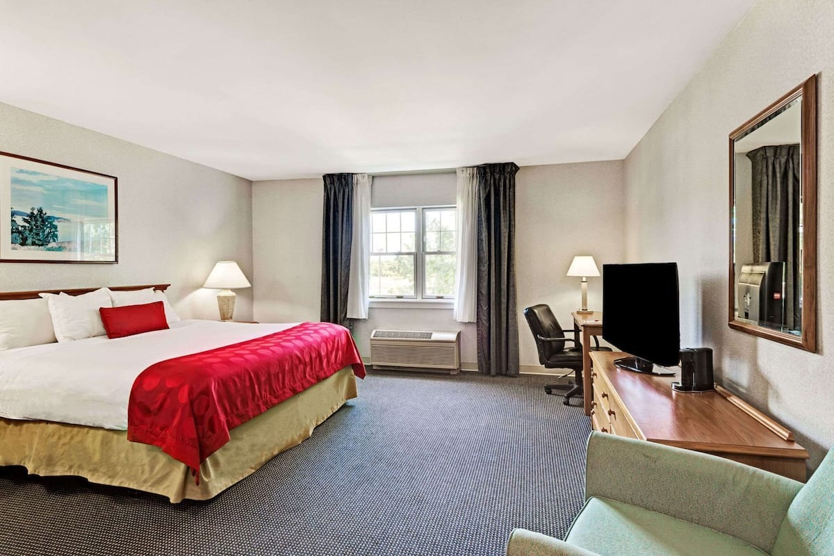 A hotel room with a bed, desk, chair, TV, and a window.