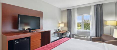 Hotellihuone, jossa on sänky, televisio, työpöytä, tuoli, lamppu ja ikkuna, jossa on verhot.
