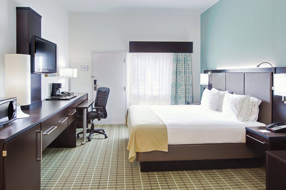 A hotel room with a bed, desk, chair, television, and a window with curtains.