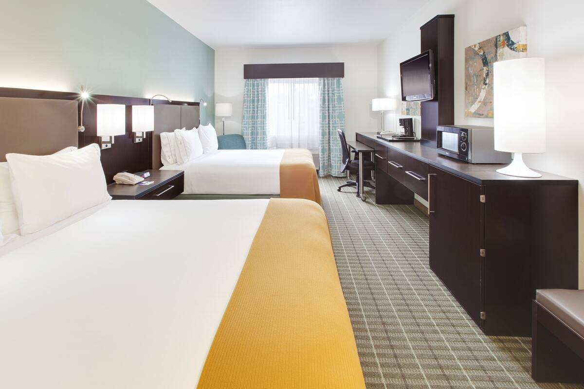 A hotel room with two beds, a desk, a TV, and a minibar.