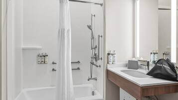 A modern bathroom with a bathtub, shower, and sink. There are toiletries on the counter and a hair dryer bag.
