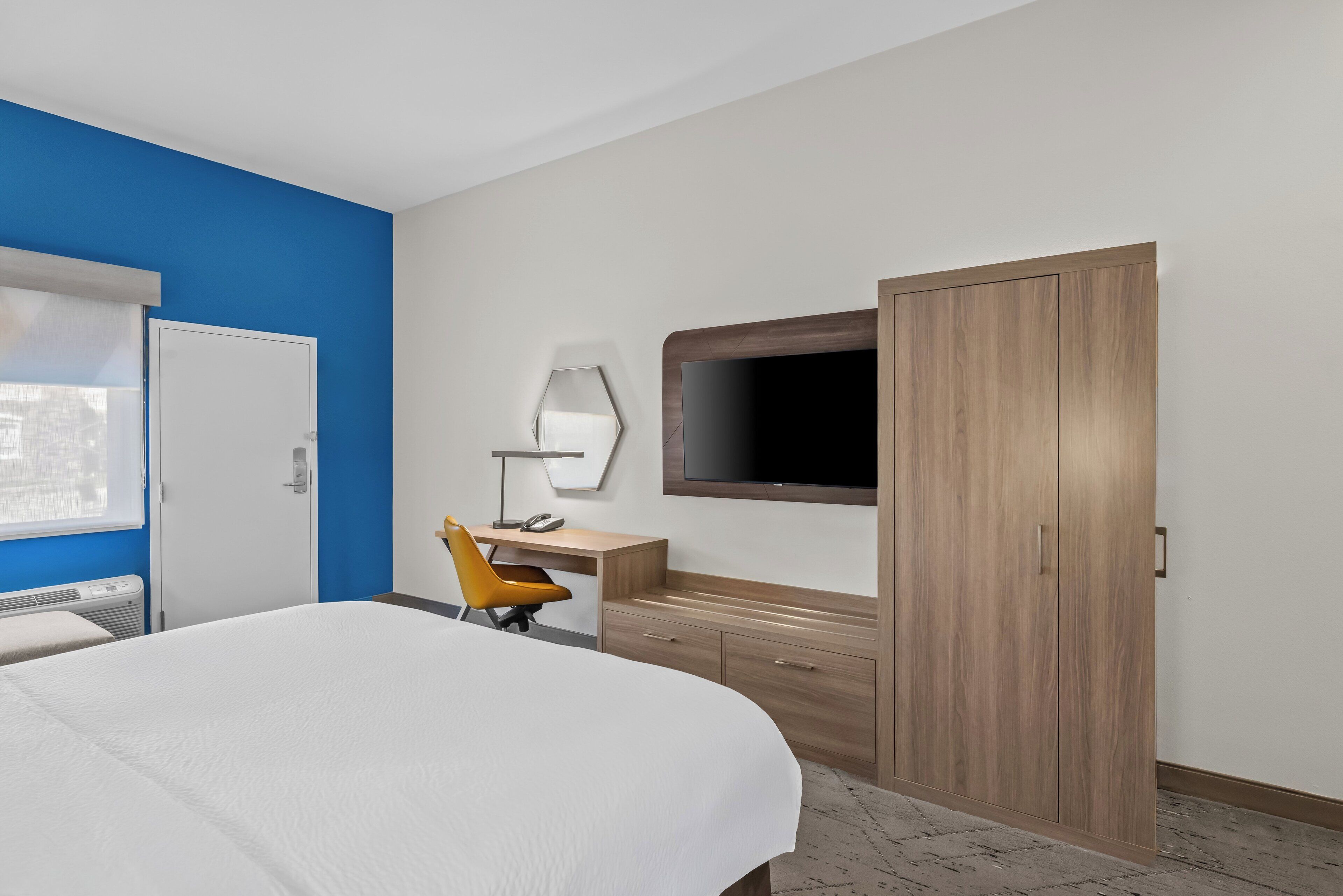Une chambre d’hôtel équipée d’un lit, d’un bureau, d’une chaise, d’une armoire et d’un téléviseur fixé au mur.
